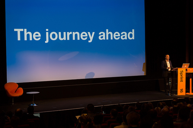 The journey ahead: Matt Hancock MP on stage with a screen reading "the journey ahead" . Photo taken at Sprint 16 GDS event