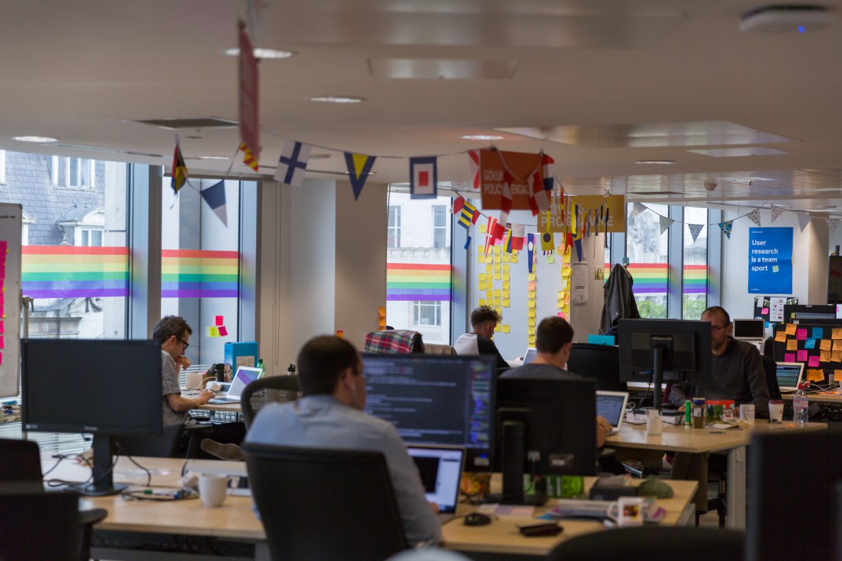 Photo of GDS offices featuring staff working at desks and the rainbow wrap stickers across the windows in the background