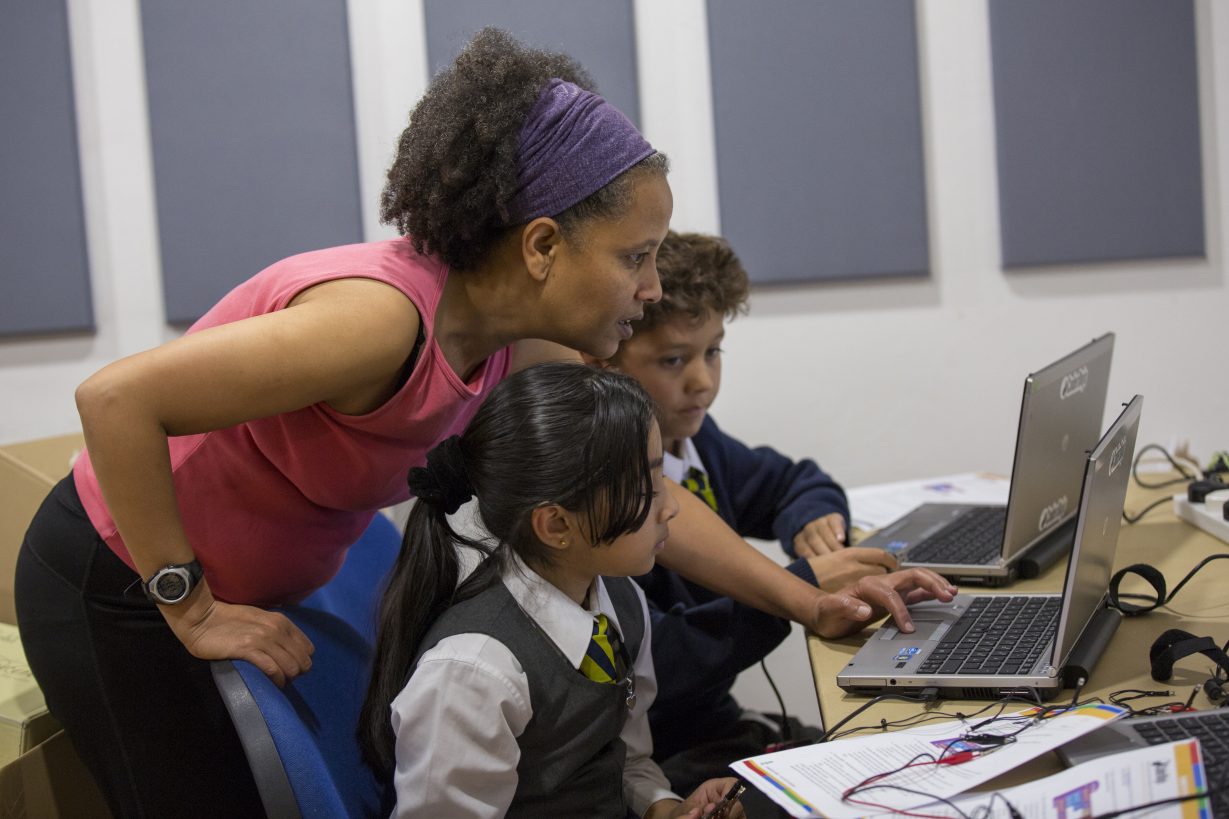 2 children being coached by an adult woman at a computer at Dragon Hall