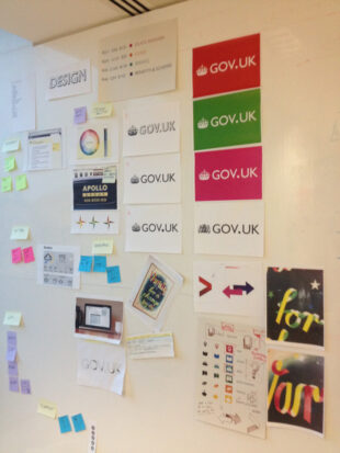 Large wall covered in various different designs of the GOV.UK logo and how that would work on a variety of backgrounds. The wall has a large sign saying Design at the top