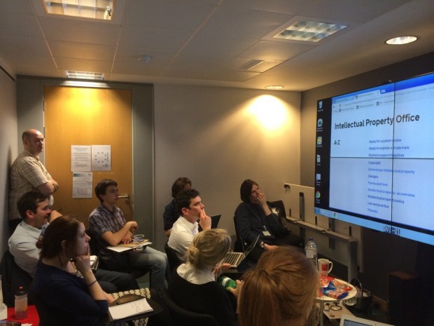 Photograph of 9 team members in the observation room at the new GDS user research lab. They are all looking at a large screen that shows a user on the Intellectual Property Office page of GOV.UK.