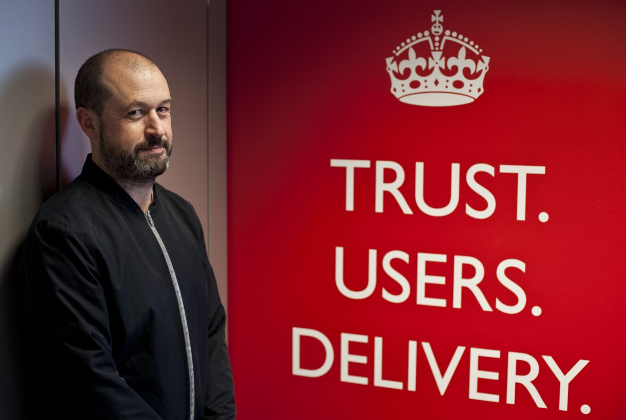 Mike Bracken standing beside a large red poster bearing the crown logo and the words ‘Trust. Users. Delivery.’