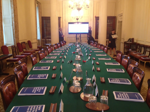 Photo of the Cabinet Room at Number 10, there is a long green table set out with paper briefing packs, iPads on stands, and a big TV screen at the end of the table ready for a meeting with GDS.