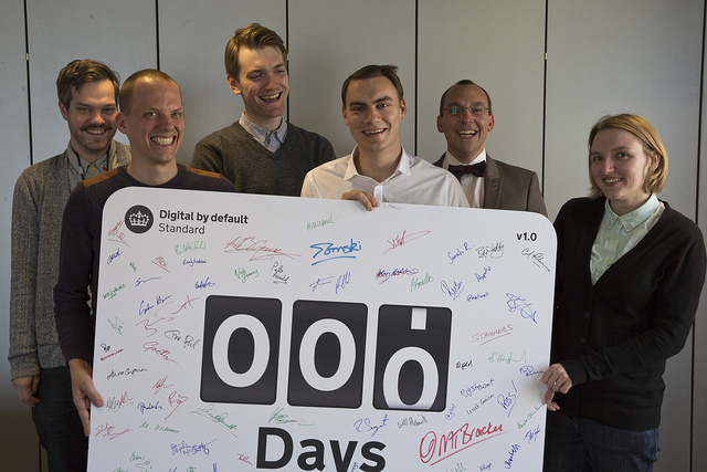 Photo of members of the team working on the Service Manual on day 0. They’re all smiling and holding a large signed board that says 000 Days.