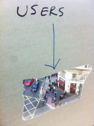 A photo of the “users” window. Someone stuck paper on a window, tore a hole in the centre of it, and wrote “Users” above it. The window (and the hole) overlooked the busy pedestrian crossing outside.