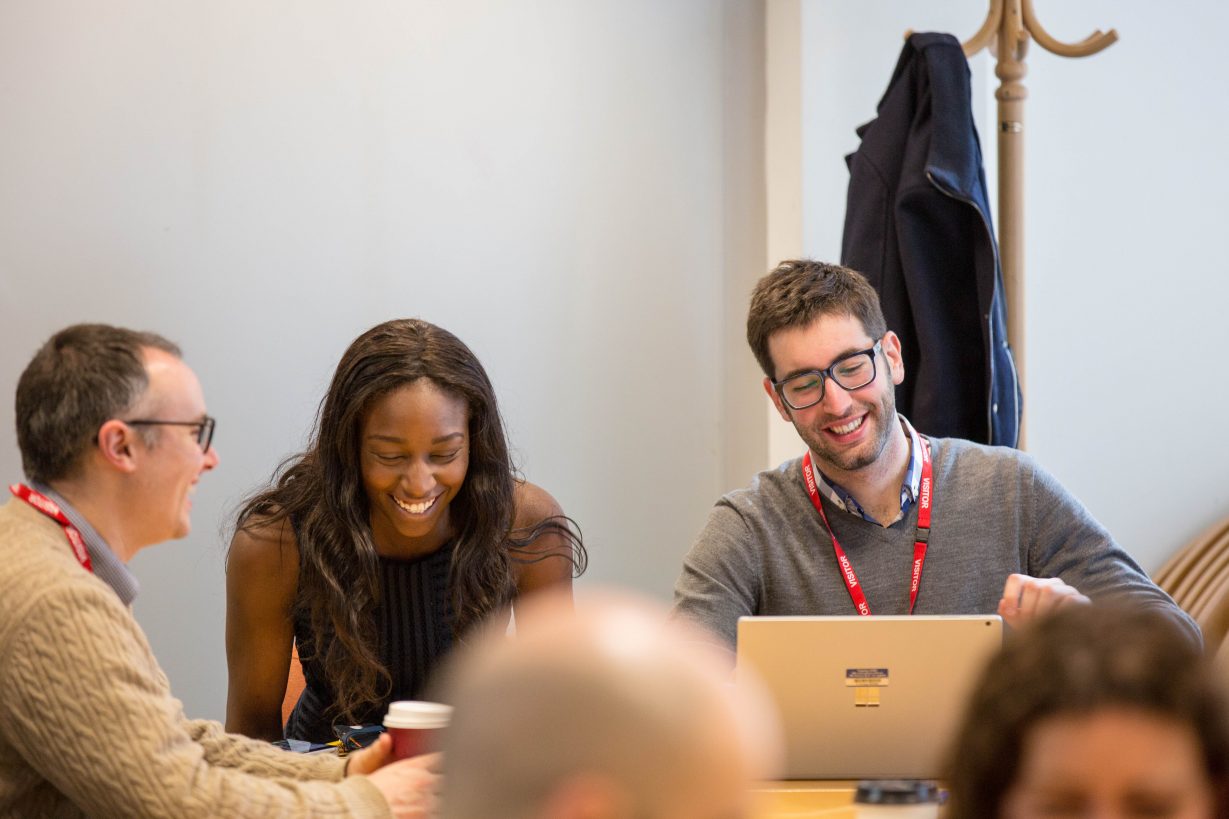 3 people sitting at a desk, looking at their laptops and smiling