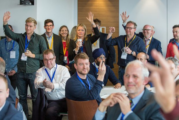 group of people listening to a talk, some of them putting their hands up