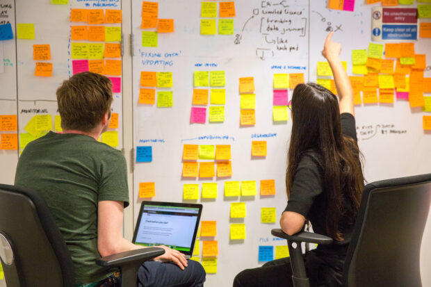 two people in front of a board with post-it notes, facing it