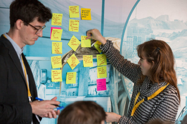 two people in front of a board putting post-it notes on it