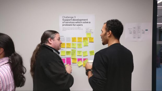 two people standing in front of a poster with post-it notes on it and talking