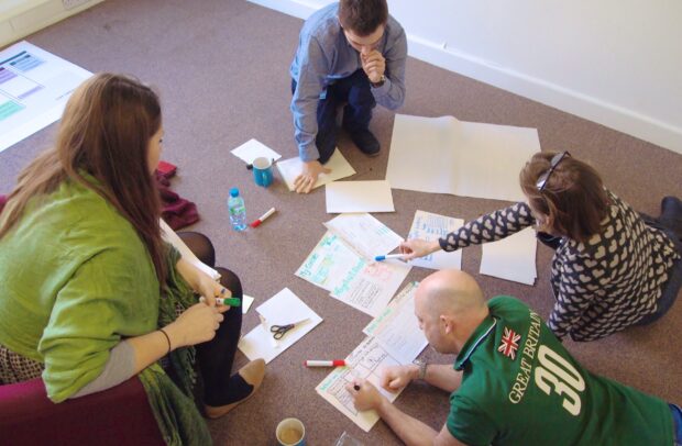 Four people sitting on the floor gathered around some sheets of paper