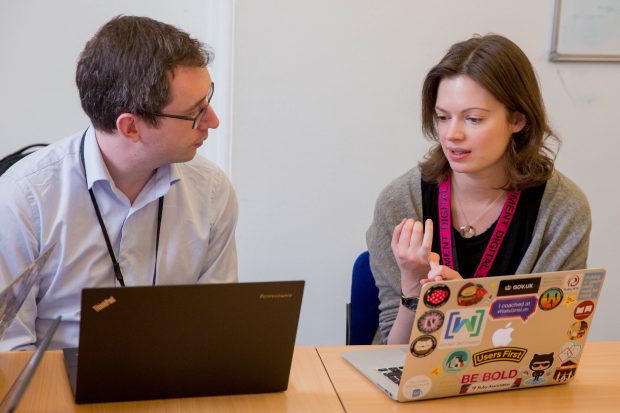 two participants of the code club discussing something, sitting at a desk with their laptops open