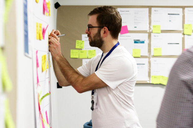 Member of staff at a design systems meet up, writing on a post-it note on a wall