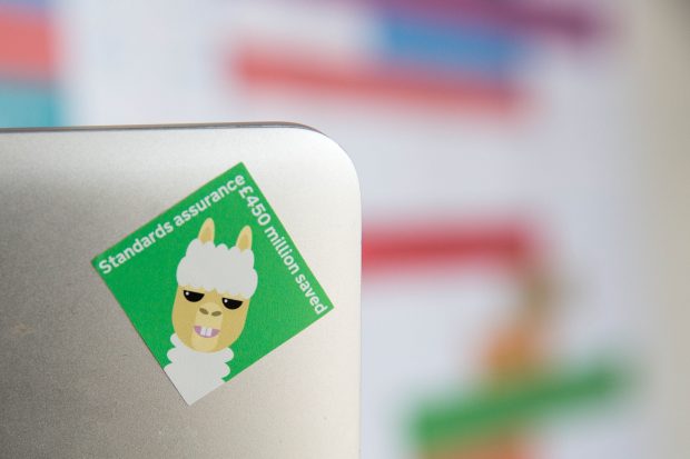 A laptop bearing a sticker showing Standards Assurance's achievement of saving £450m