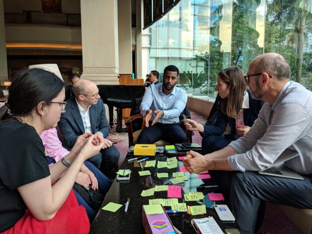 6 people sitting around a table and talking, the table is covered with post-it notes