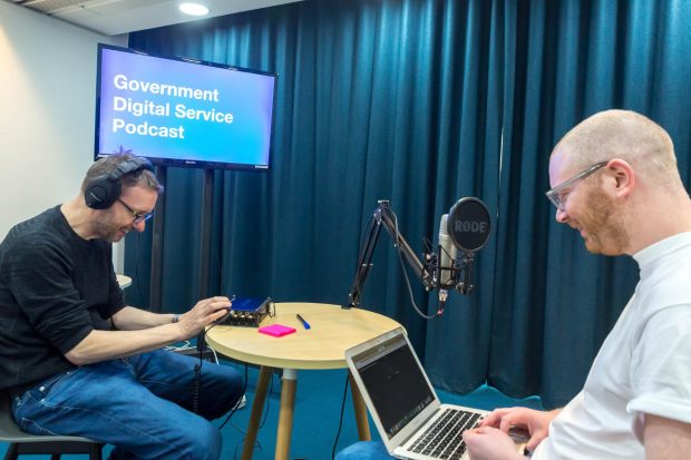 Two members of the GDS creative team in a studio, with a microphone, looking at their laptops