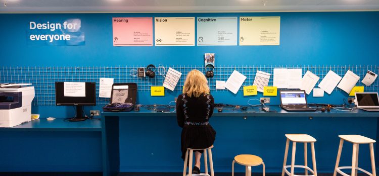 The GDS accessibility lab - a blue wall with a table with laptops and other devices on it. A user sitting at the table doing some work.