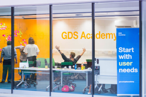 Photo of the GDS Academy classroom and person celebrating. 3 other people standing by the way and looking at post-it notes stuck to it