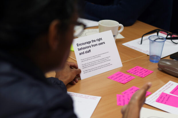 the back of a person sitting at a desk with some post-it notes on it, and a card that says 'encourage the right behaviours from users and staff'