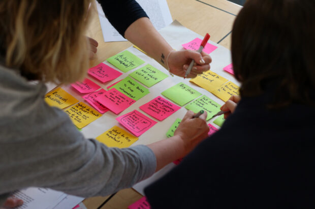 group of people writing on post-it notes, which are attached to a sheet of paper on a table