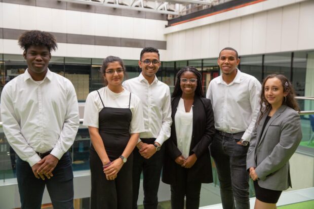 6 people standing, facing the camera and posing for a picture