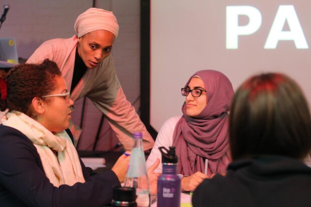 three people looking at each other and talking, one of them is standing