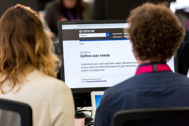 2 people facing away from the camera and looking at a screen showing a page on GOV.UK saying 'Define user needs'