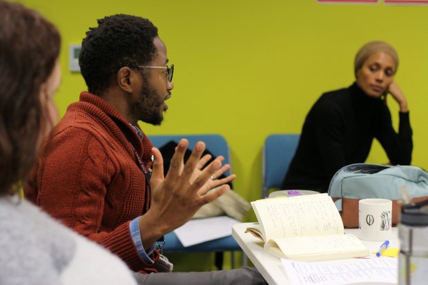 a person sitting at a table discussing something, two other people listening