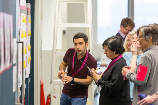 group of people standing in front of a board and looking at the post-its on it