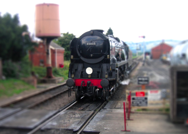 Black steam train approaching a foot crossing. 