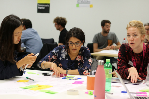 Various people participating in service design training. Three young women in the front are collaborating on a task, using colourful sticky notes