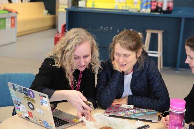 Laura Stevens and Charlotte Downs, Creative Content Producers at GDS sitting next to a female colleague sitting at a table, looking curiously at a screen