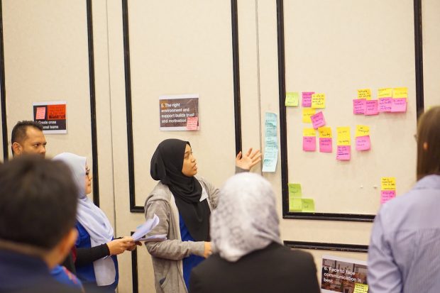 People are looking at sticky notes on a wall that contain notes.