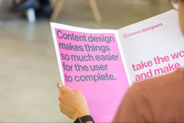 A person is holding a printed booklet. The left page reads "Content design makes things so much easier for the user to complete." The right page reads incomplete text.