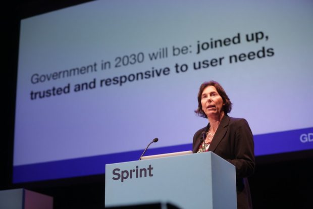 Alison Pritchard stands at a Sprint-branded lectern, and on the screen behind her is the text "Government in 2030 will be: joined up, trusted and responsive to user needs".