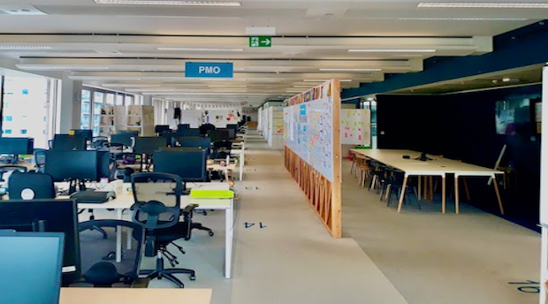 Empty work spaces at the GDS offices showing rows of desks and whiteboards with post-it notes.