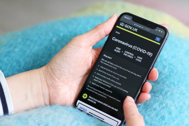 A hand holds a mobile device showing the GOV.UK coronavirus landing page.