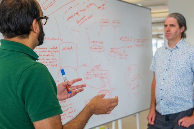 Two people are discussing a concept map on the whiteboard they are standing next to.