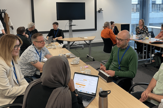 A group of people sitting around a table with one laptop being used.