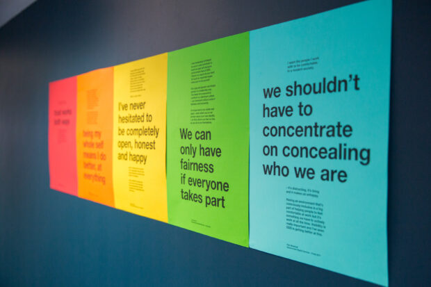 Five posters, ordered chromatically from red to teal from left to right. Their subject matter is regarding encouraging openness in the workplace, and being true to oneself.