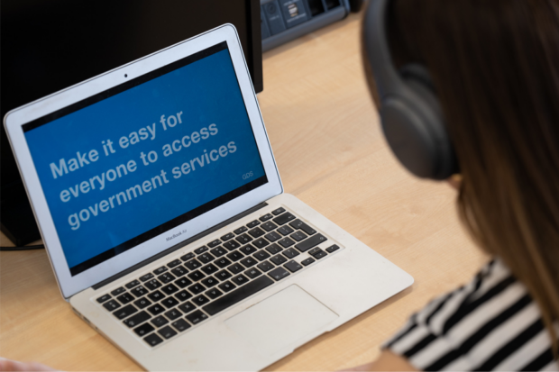 A person looking at a laptop screen which shows a GDS presentation slide. The text says "Make it easy for everyone to access government services".