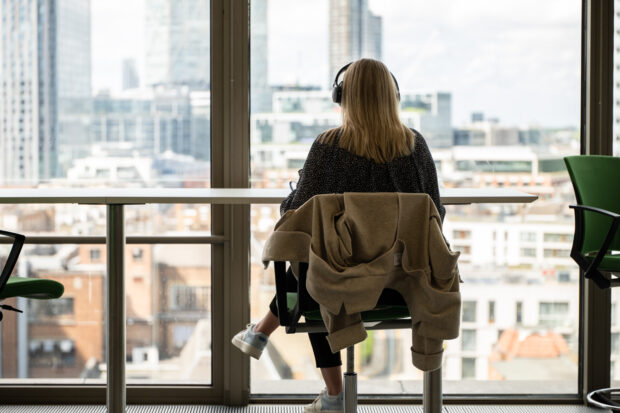 A person wearing a headphone sitting down facing the window inside the office.