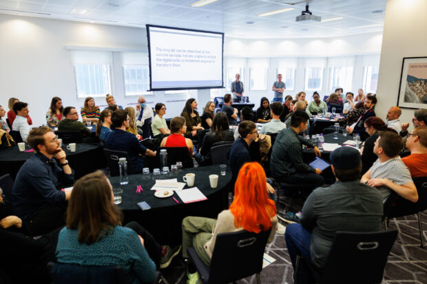 A large group of people discussing a slide titled: “The long tail can be described as low volume services that are unable to access the digital skills or investment required to transform them"