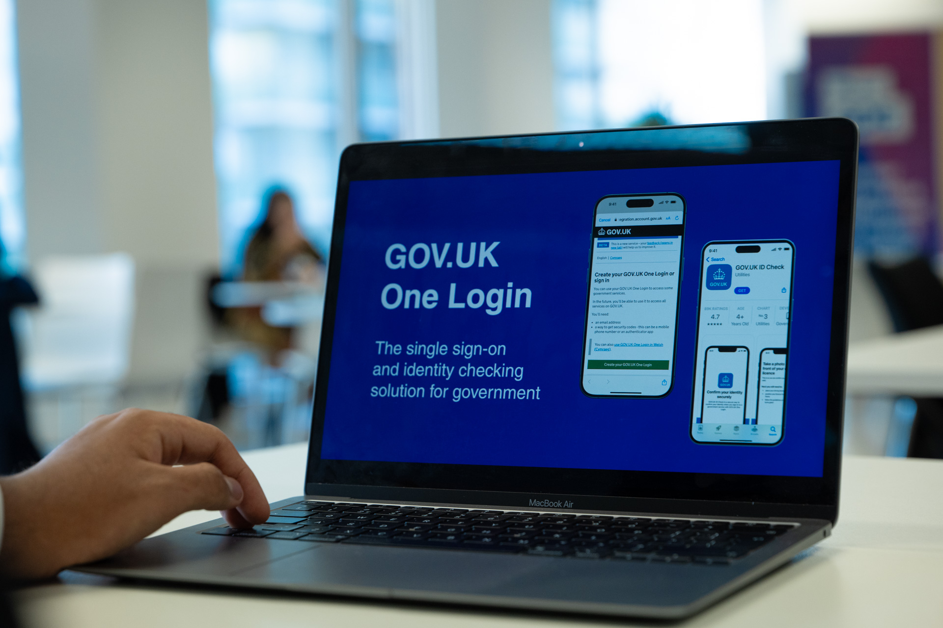 The image features a person with their hand on the keyboard of a laptop. The laptop screen displays: ‘GOV.UK One Login the single sign-on and identity checking solution for government’.