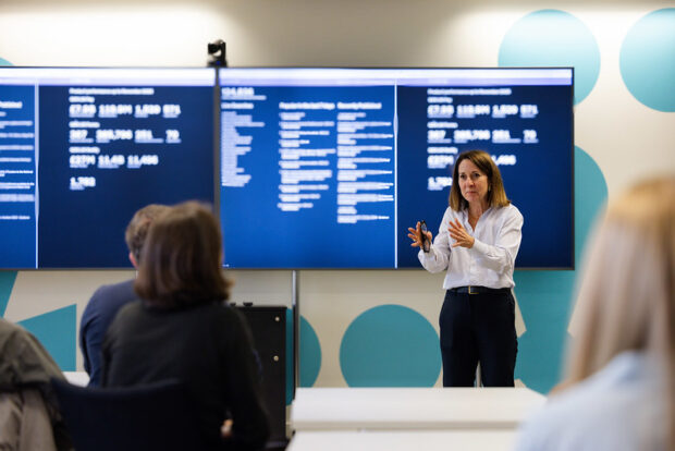 Liz Kendall, Secretary of State for Science, Innovation and Technology presenting data on large screens to an attentive audience in a modern conference room. The setting is professional and engaging.