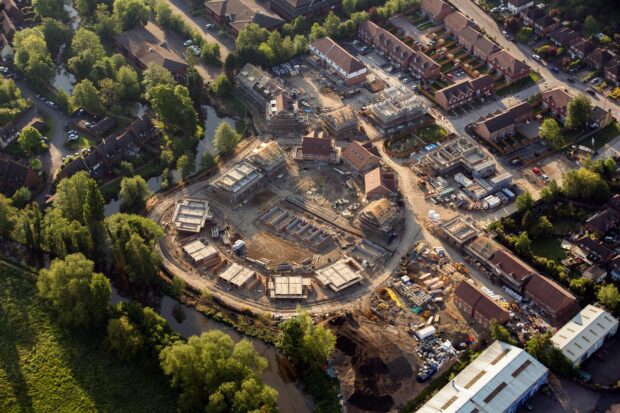 Aerial photograph of a residential housing development in progress, showing new homes under construction alongside established neighbourhoods and green spaces.