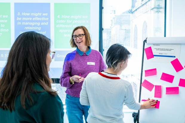 Workshop participants reviewing and adding sticky notes to a flip chart during a collaborative session.